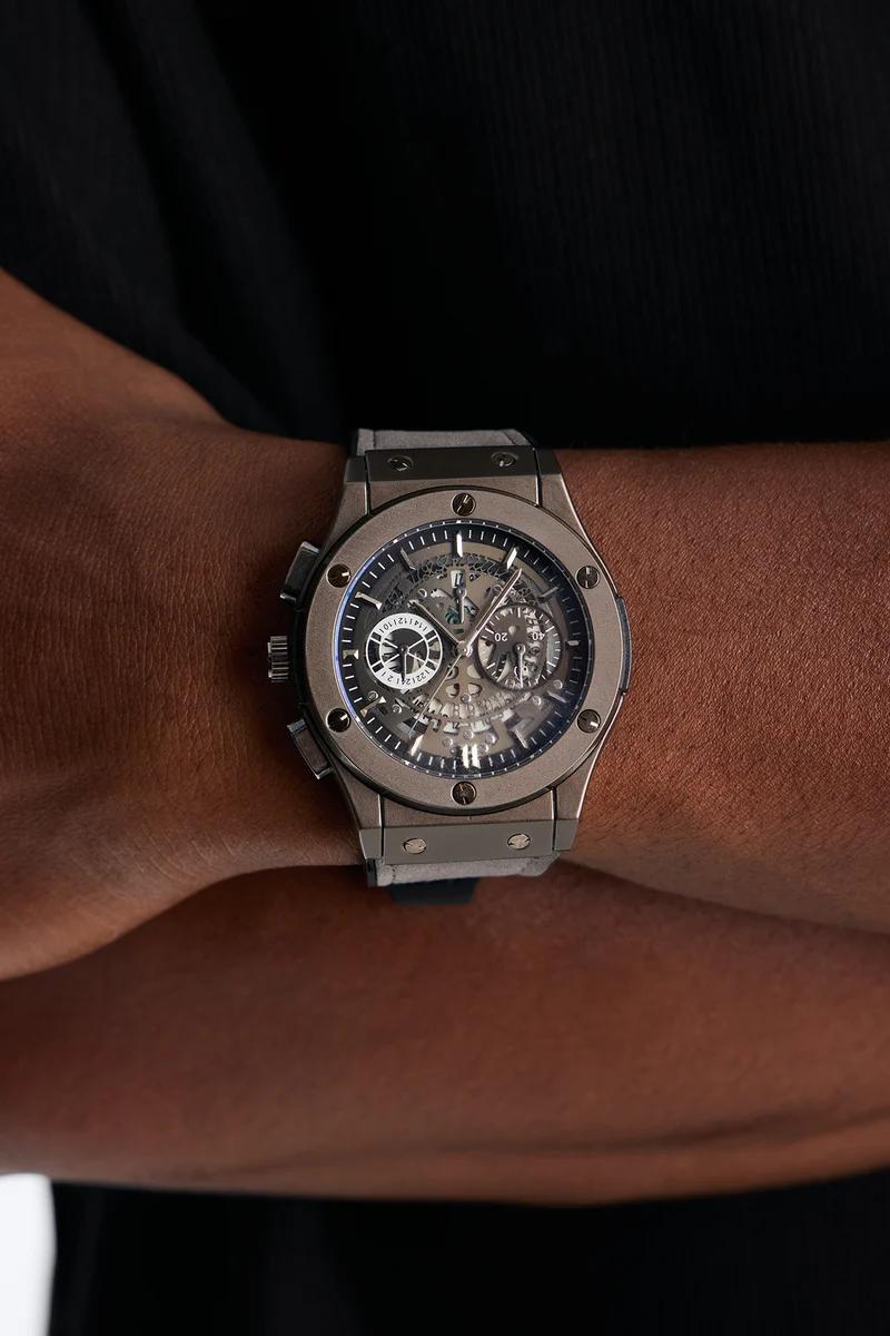 Primer plano de un reloj cronógrafo de lujo de titanio con esfera esqueletizada y correa gris claro, llevado en la muñeca. Mostrando elegantes relojes de hombre.