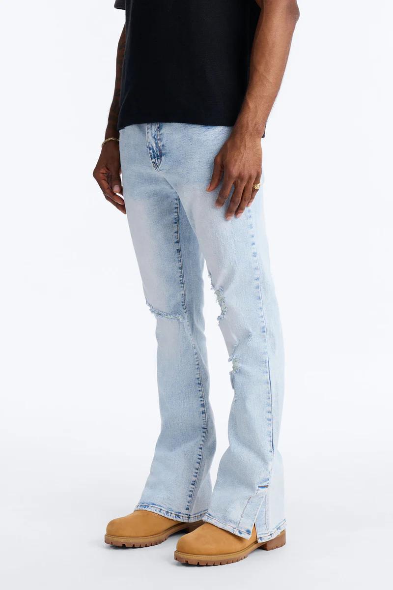 Hombre viste jeans flare desgastados azul claro con aberturas y botas tan, mostrando nuestra nueva colección denim casual.