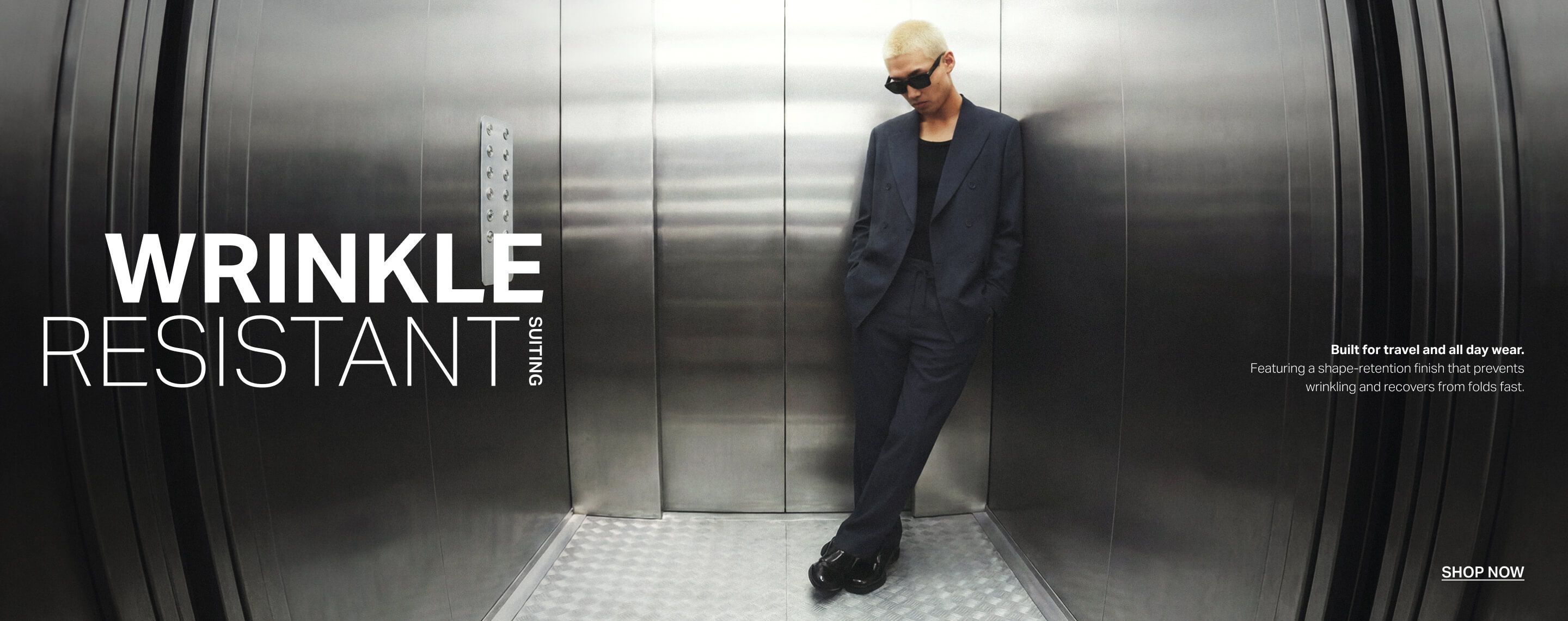 Man in a modern navy men's dress suit and sunglasses in an elevator. Shop travel-friendly, wrinkle-resistant suits for daily wear.