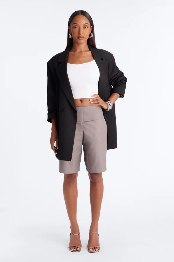 Model in an oversized black blazer, white crop top, and taupe tailored shorts showcases a chic women's smart-casual summer fashion collection.