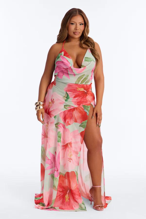 Woman in a mint green plus size floral maxi dress with pink/red hibiscus print, cowl neck, and leg slit, ideal for summer.
