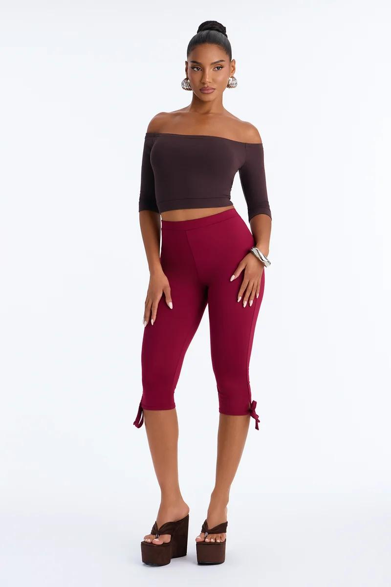 Woman wearing a brown off-the-shoulder crop top and burgundy capri leggings with platform sandals.