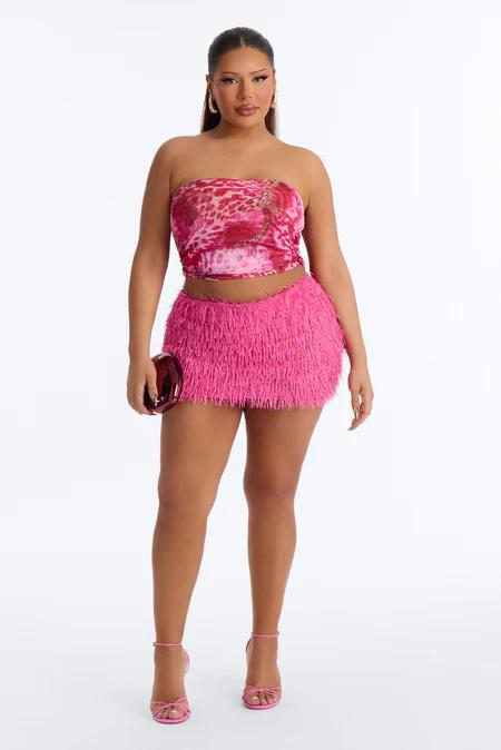 Mujer con top rosa de leopardo, minifalda rosa de flecos, tacones a juego, y bolso de mano rojo. Con pendientes dorados.