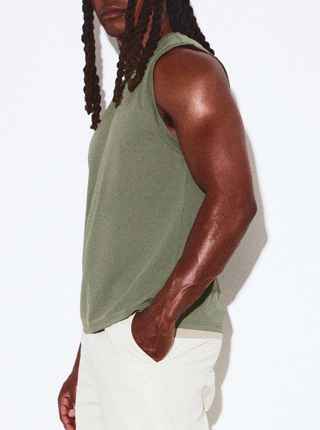 Man in olive green tank top and light pants, hand in pocket, showcasing comfortable men's casual summer wear.