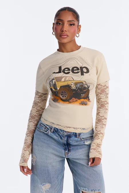 Woman in a beige Jeep graphic tee with a yellow Wrangler over a lace long-sleeve shirt and distressed blue jeans, looking forward.