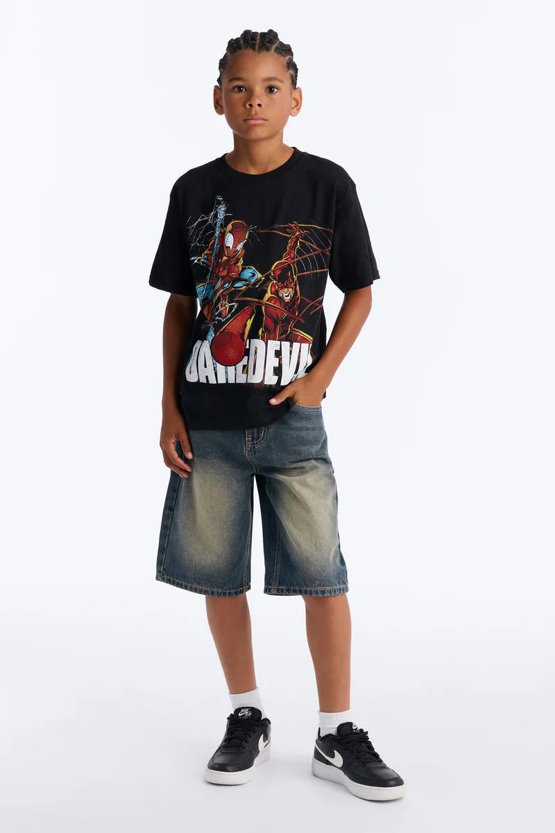 Boy wearing Marvel Spider-Man Daredevil t-shirt, distressed denim shorts, and black Nike sneakers. Kids fashion.