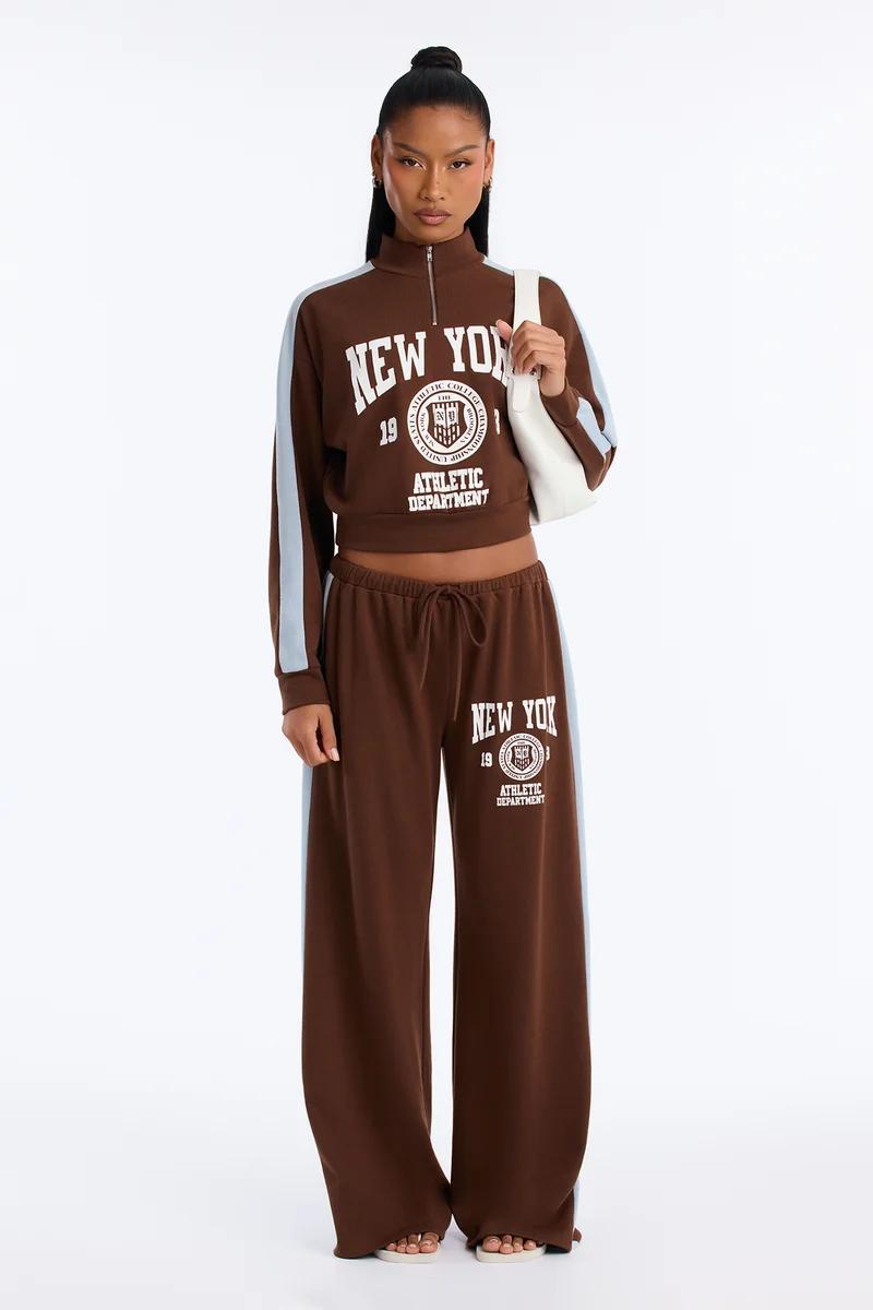 Woman in brown graphic cropped sweatshirt and matching wide-leg sweatpants set with light blue side stripes.