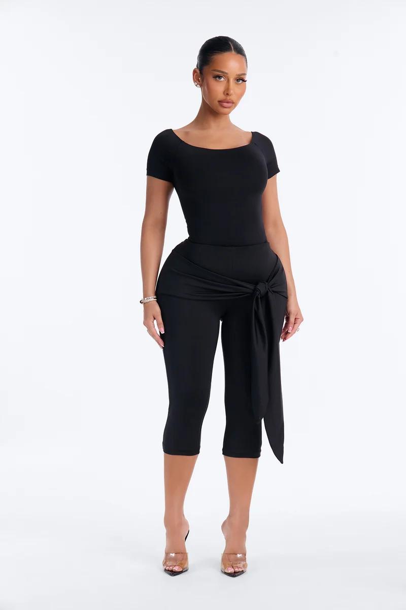 Woman wearing a black short-sleeve top and matching tie-waist capri pants set.
