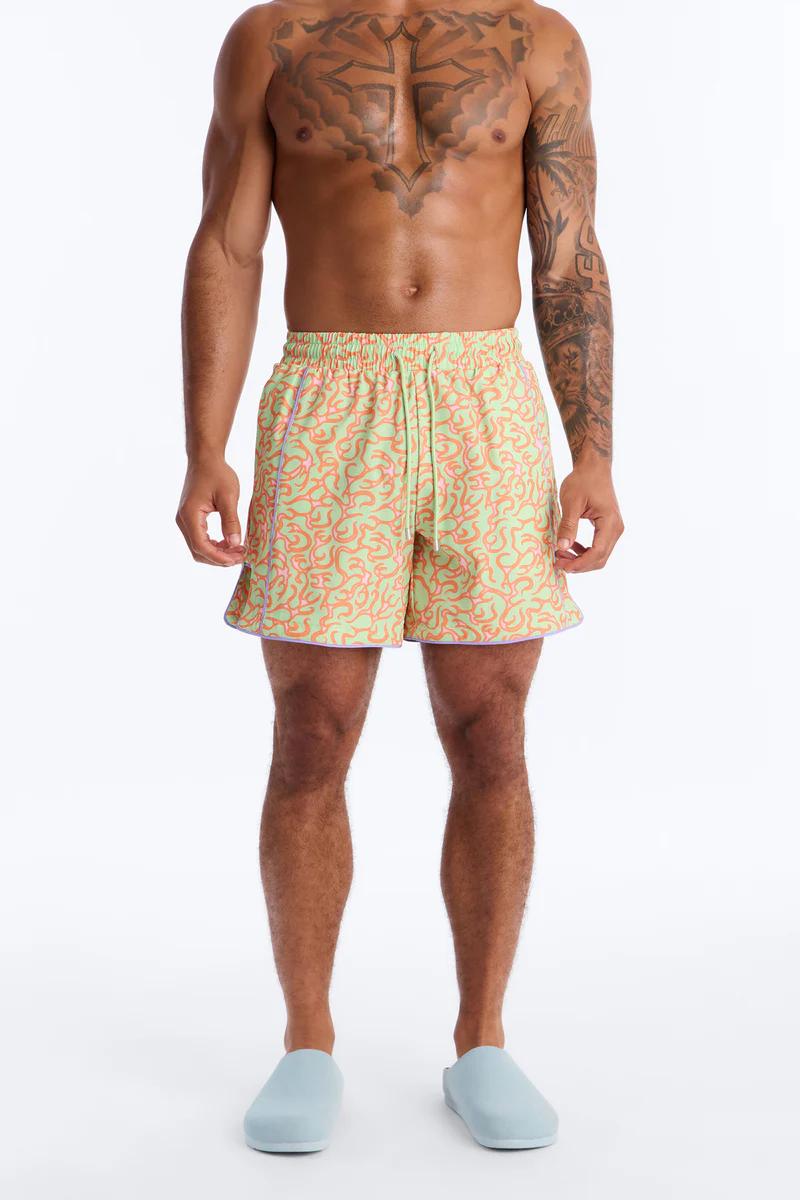 Man modeling light green patterned swim shorts with orange/pink swirls and purple trim. Perfect men's summer shorts for beachwear or resort.