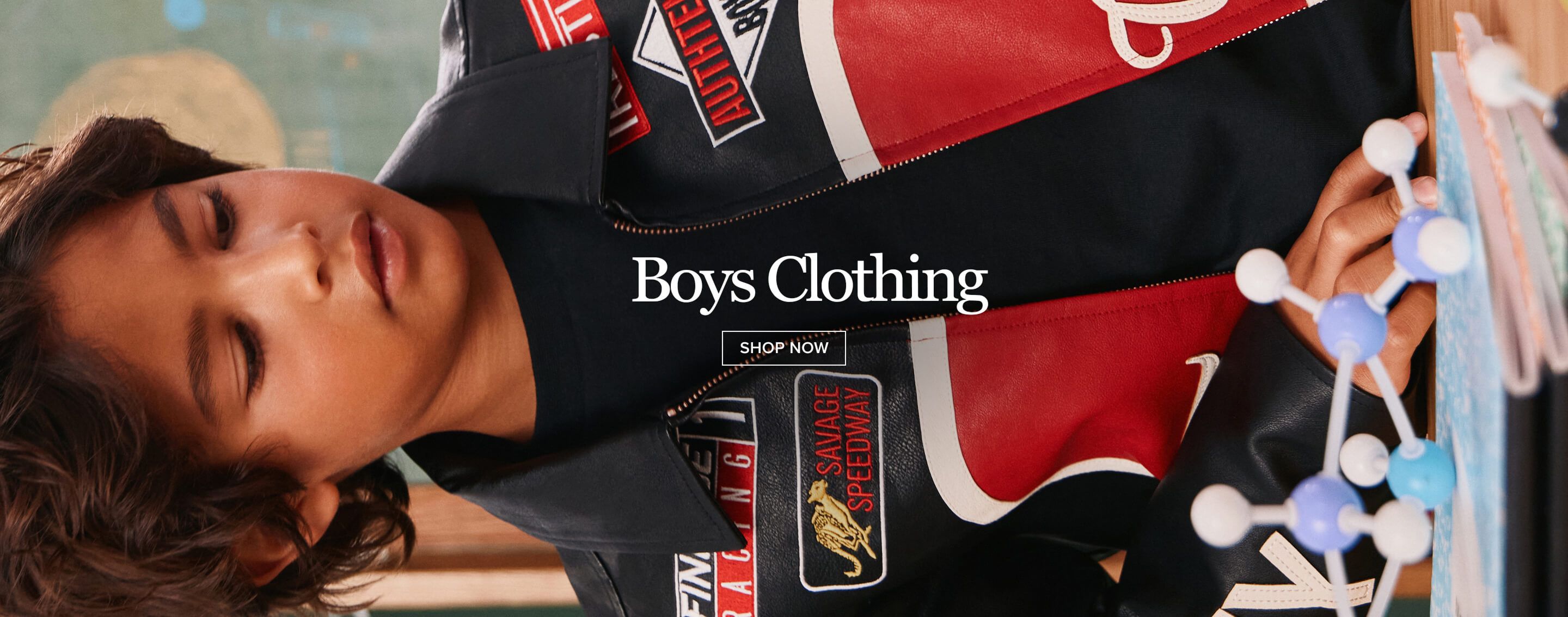 Boy in a stylish black, red, and white racing jacket with patches, looking at a molecular model. Shop new boys clothing fashion.