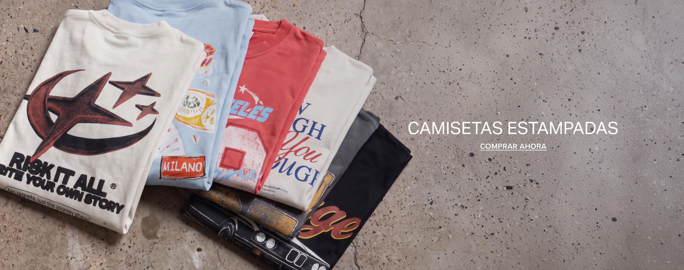 Pila de camisetas gráficas de estilo urbano sobre concreto, promoviendo una compra de playeras y camisetas estampadas de moda.