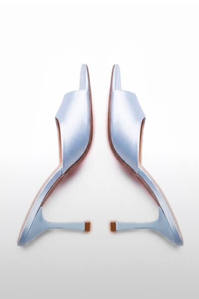 Elegantes mules de raso azul claro con tacones bajos, suelas enfrentadas sobre blanco, promocionando calzado femenino chic.