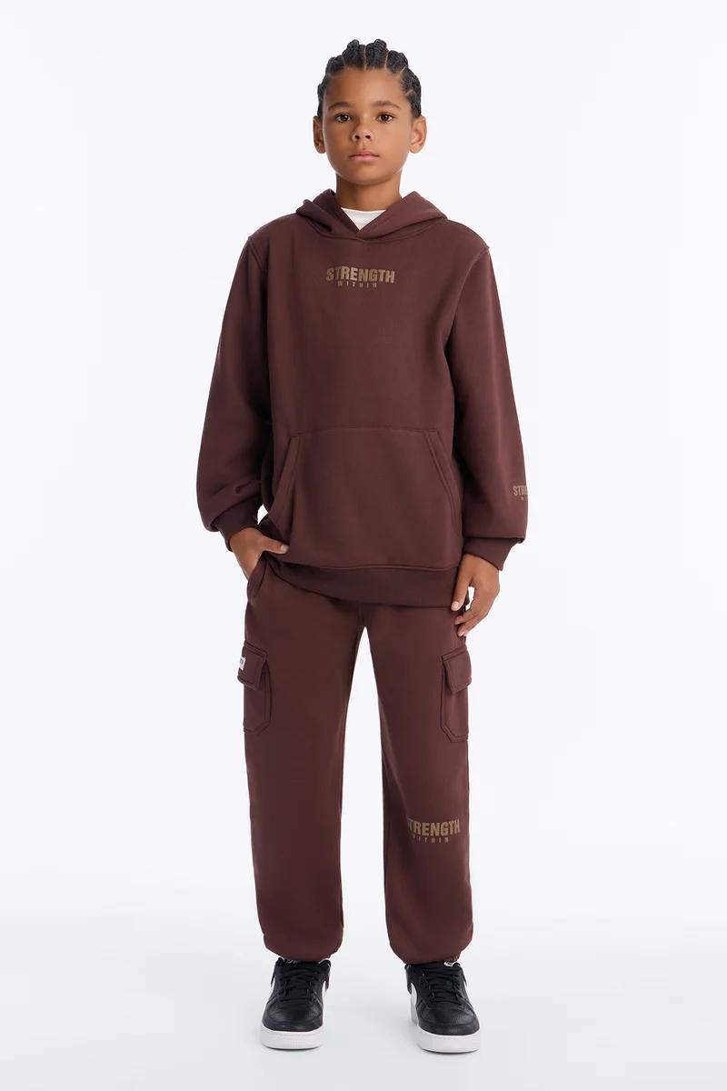 Young boy wearing a brown hoodie and matching cargo sweatpants tracksuit set.