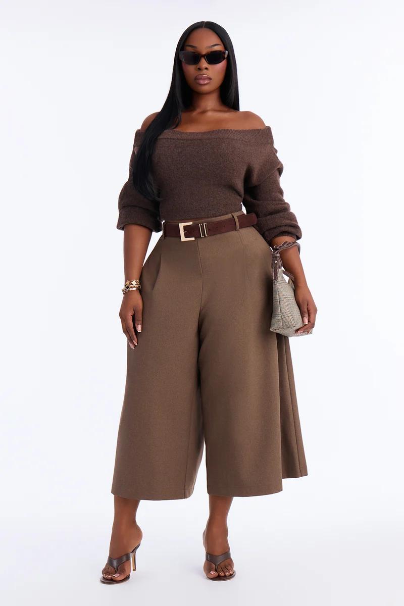 Woman in an off-the-shoulder brown knit sweater, high-waisted wide-leg culottes, belt, sunglasses, and heels.