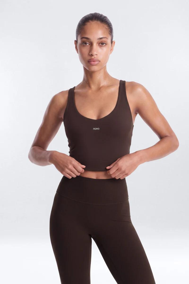 Model wears dark brown Nova cropped sports top and matching high-waisted activewear leggings, showcasing a sleek fitness set.