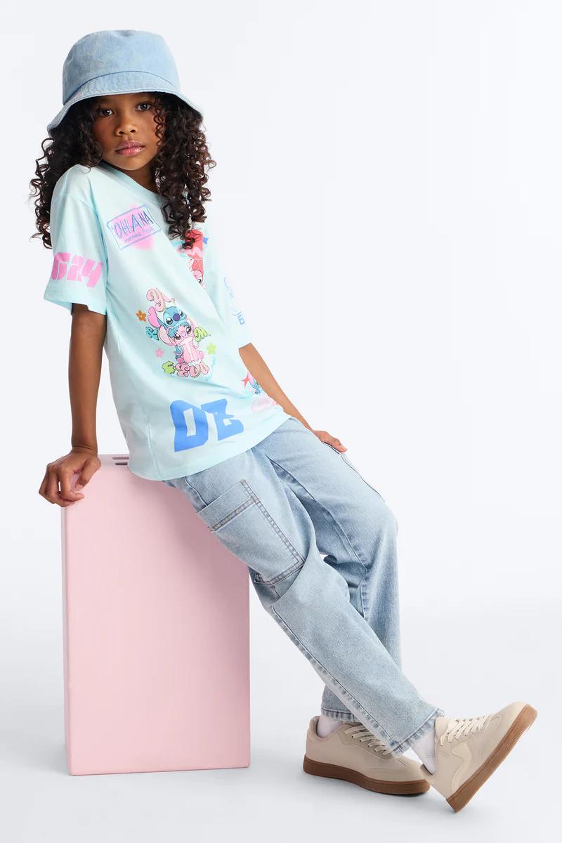Girl in Lilo & Stitch 'Ohana' tee, denim cargo pants, bucket hat, sneakers. Kids fashion.