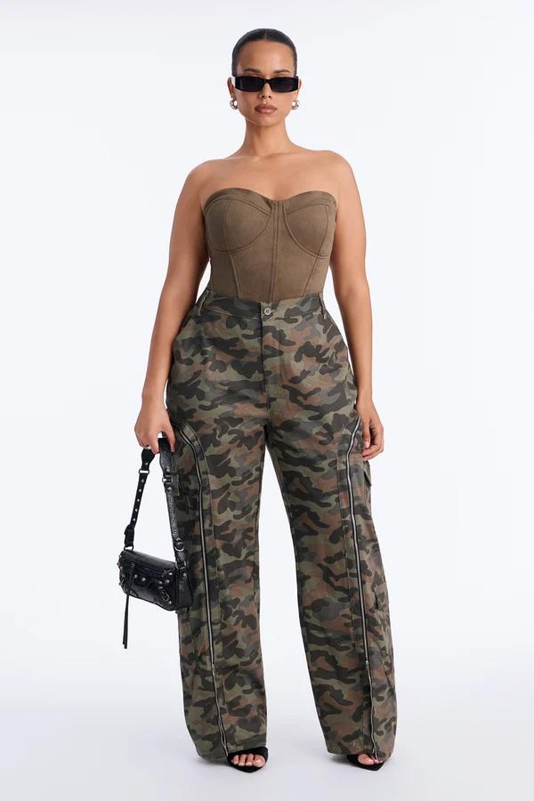 Curvy model posing in a brown strapless corset top and green camouflage cargo pants with a black handbag for a trendy streetwear collection.