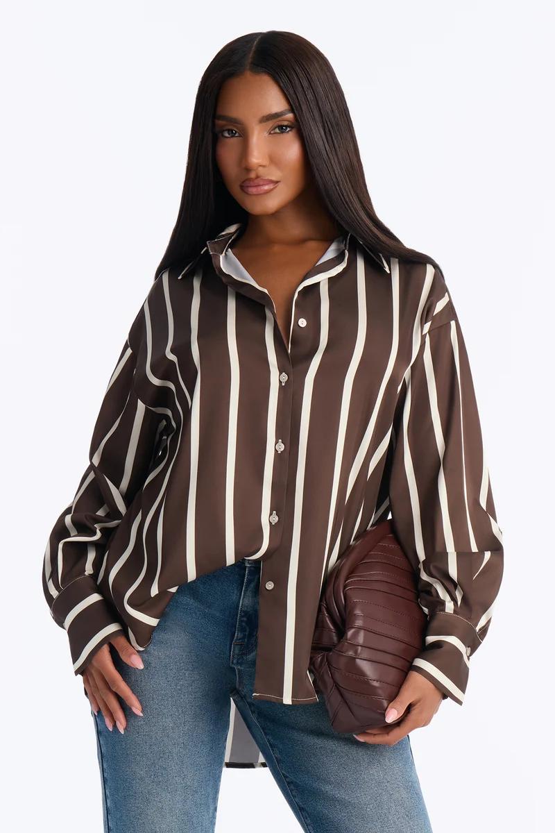 Mujer con camisa de rayas marrón y blanca, vaqueros azules y un bolso de mano marrón.