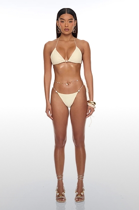 Model in a cream triangle bikini, delicate pearl body chain, and gold strappy heels, showcasing stylish new swimwear.