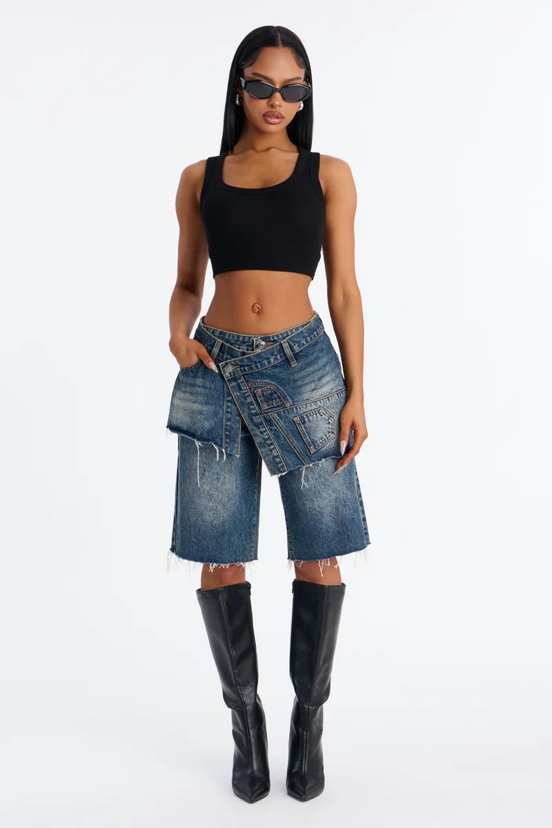 Woman wearing a black crop top, asymmetrical denim bermuda shorts, knee-high black boots, and sunglasses.