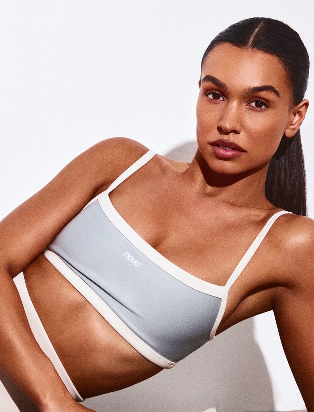 Woman wearing a light blue and white Nova sporty bikini top from the new swimwear collection, posing against a clean white background.