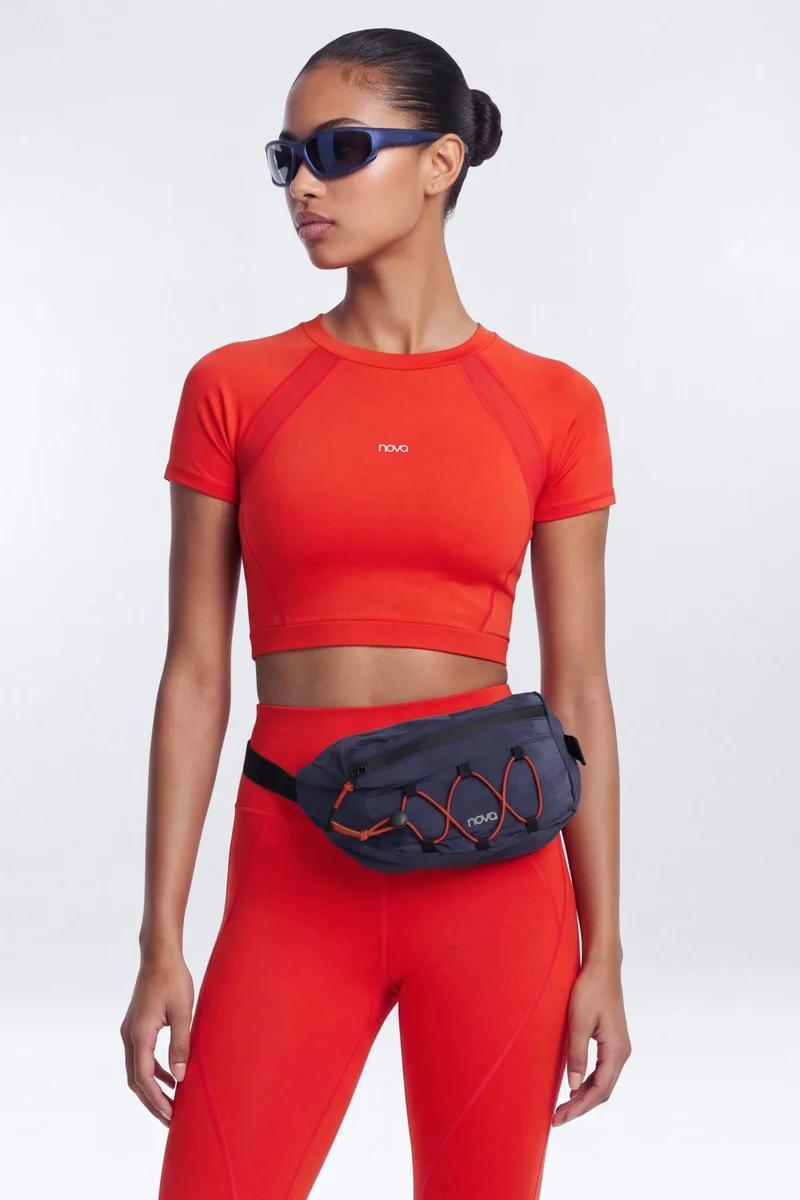 Woman modeling bright red athletic crop top and leggings set paired with a dark blue belt bag from the new Nova sport collection.
