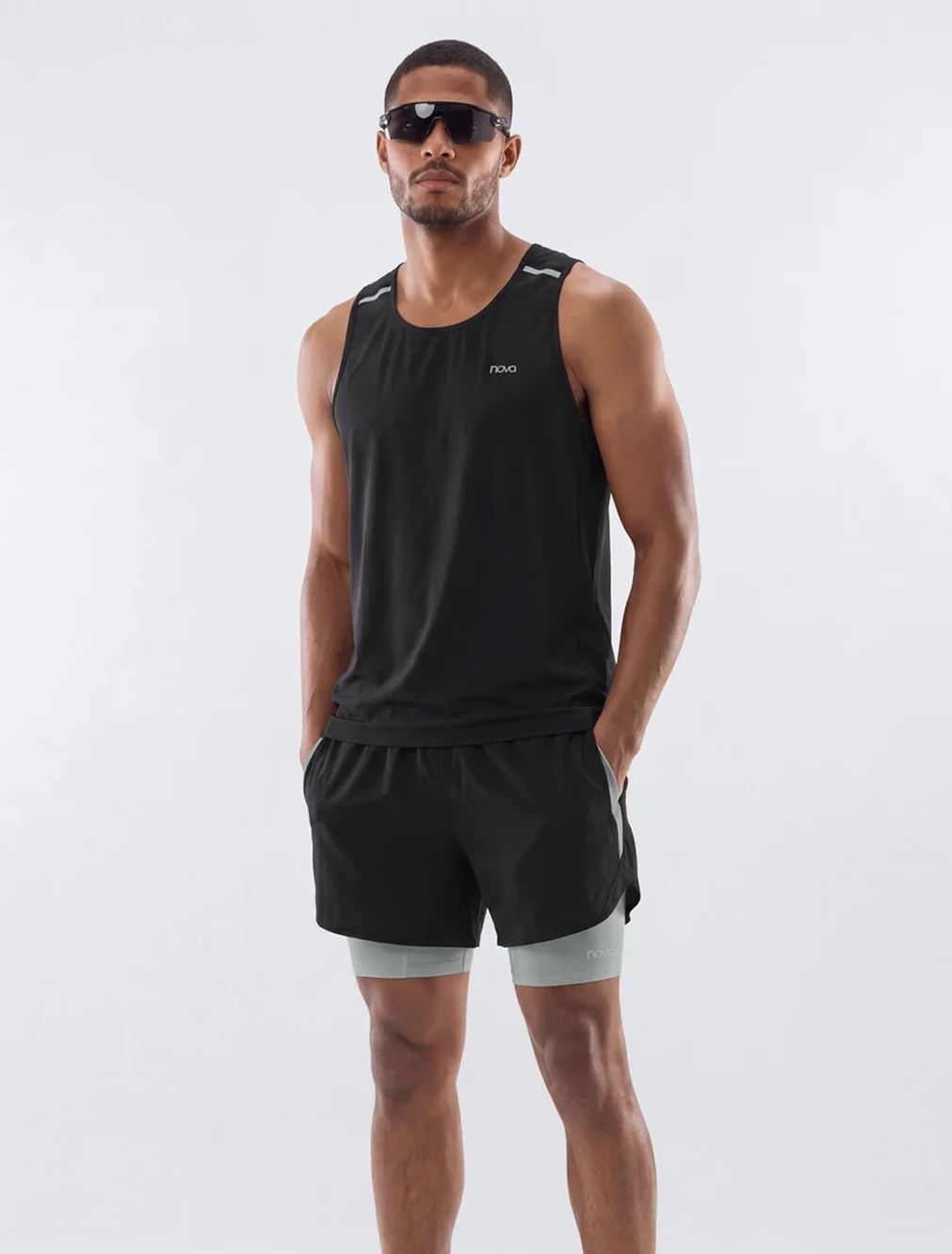 Man wearing sunglasses and Nova men's activewear, showcasing a black running tank top and matching shorts with a grey compression liner.