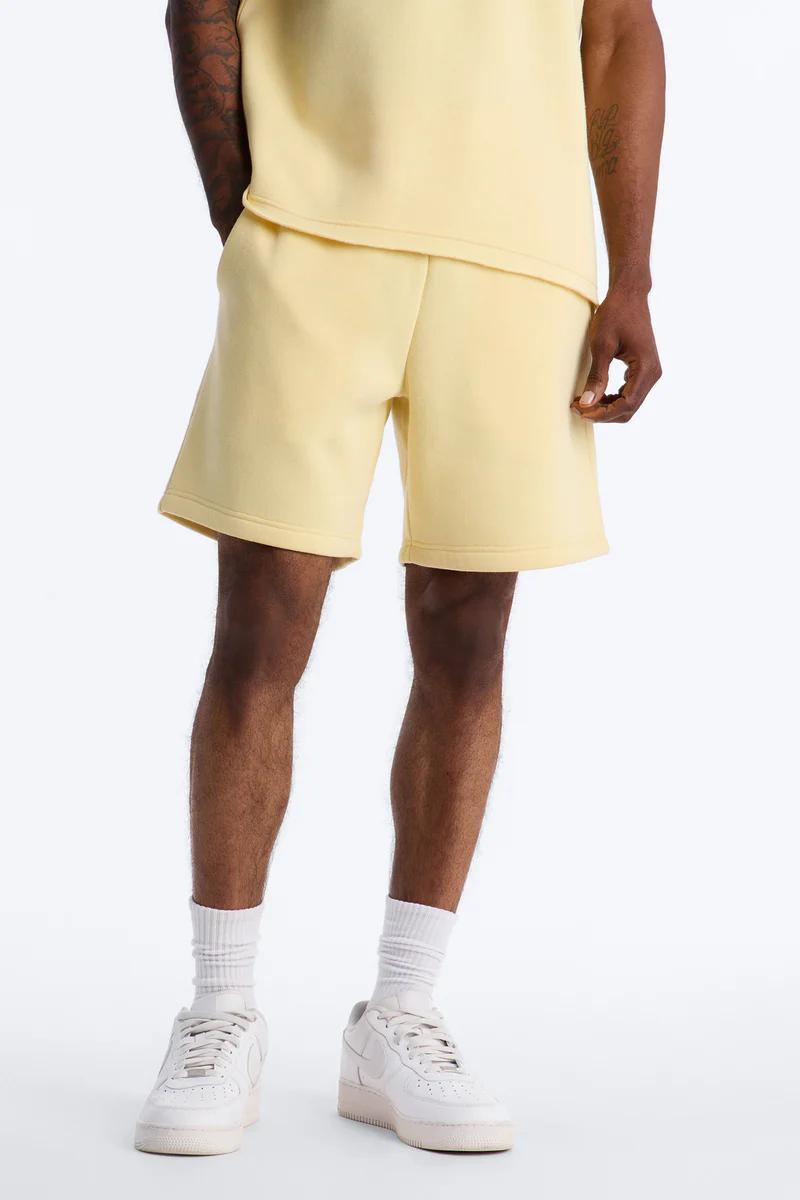Model in pale yellow fleece sweat shorts and matching sweatshirt, showcasing a comfortable men's casual outfit.
