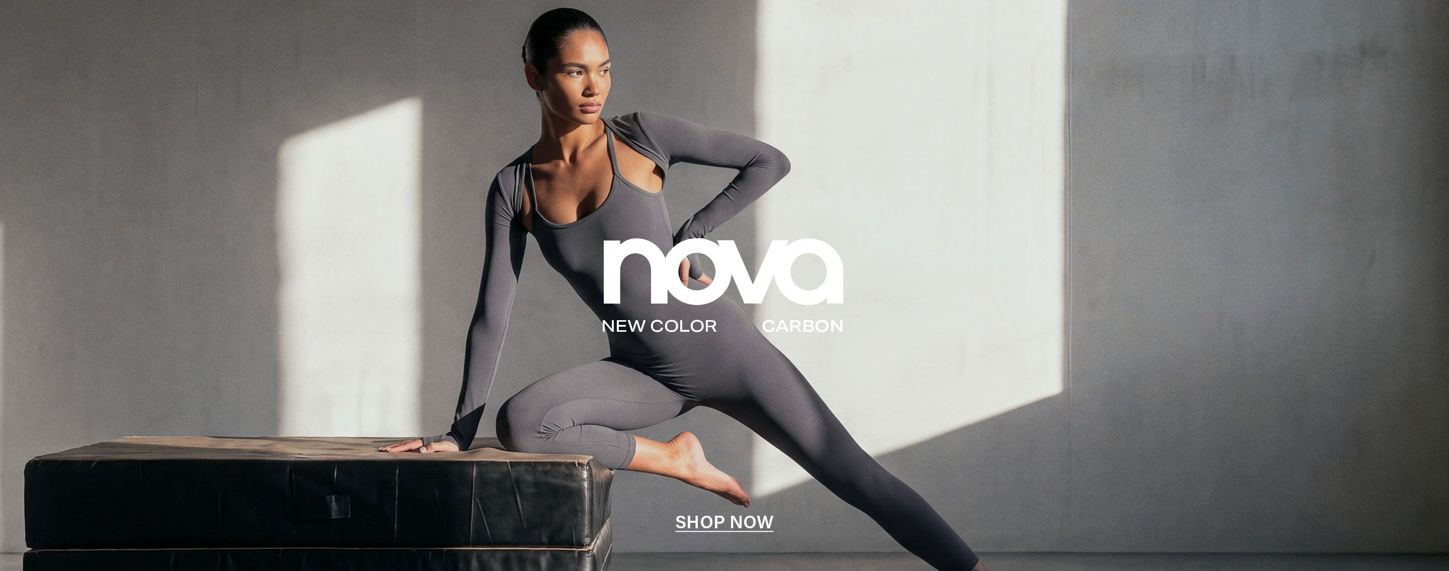 Model strikes a dynamic pose in a gray Nova activewear jumpsuit, promoting the brand's new carbon color fitness apparel collection.