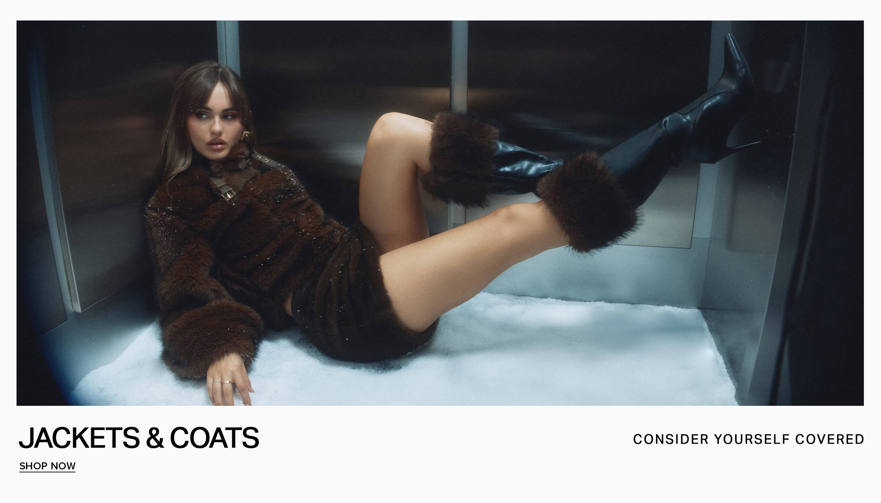 Model in a dark brown faux fur jacket leaning against a modern wall to promote the jackets and coats category, inviting users to shop now.
