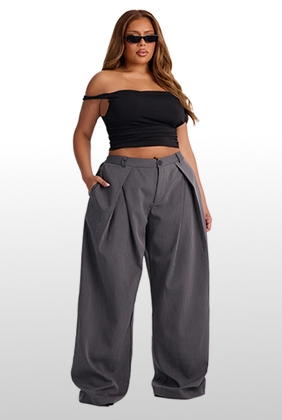 Plus size model wears trendy grey wide-leg pleated trousers and a black off-the-shoulder crop top for a modern streetwear collection.