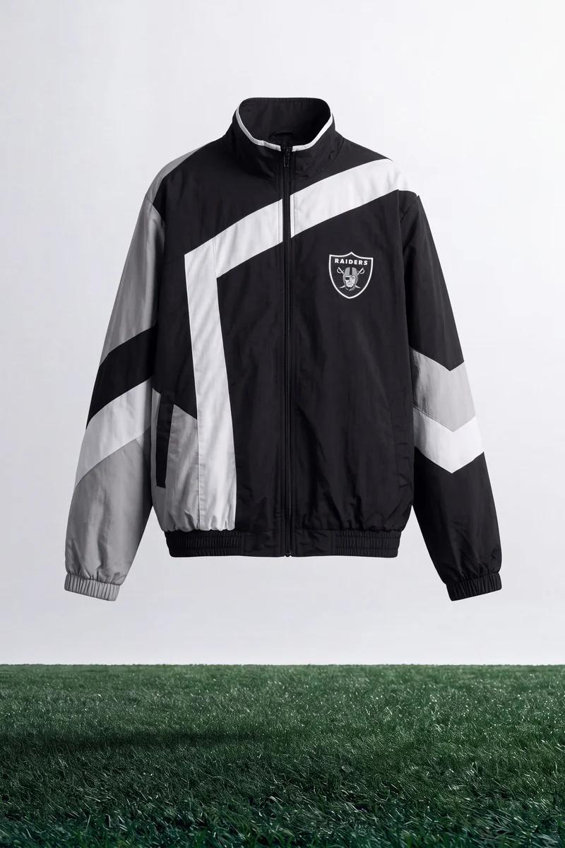 Stand-alone black, white, and grey Raiders windbreaker jacket featuring bold geometric stripes. Essential NFL fan apparel for modern sports fashion.