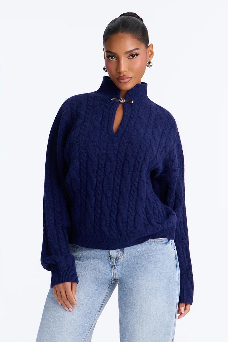 Woman wearing a navy blue cable knit mock neck sweater with a keyhole cutout and gold hardware, paired with light blue jeans.