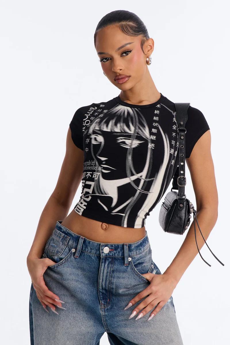 Woman wearing a black Y2K anime graphic crop top and blue jeans.