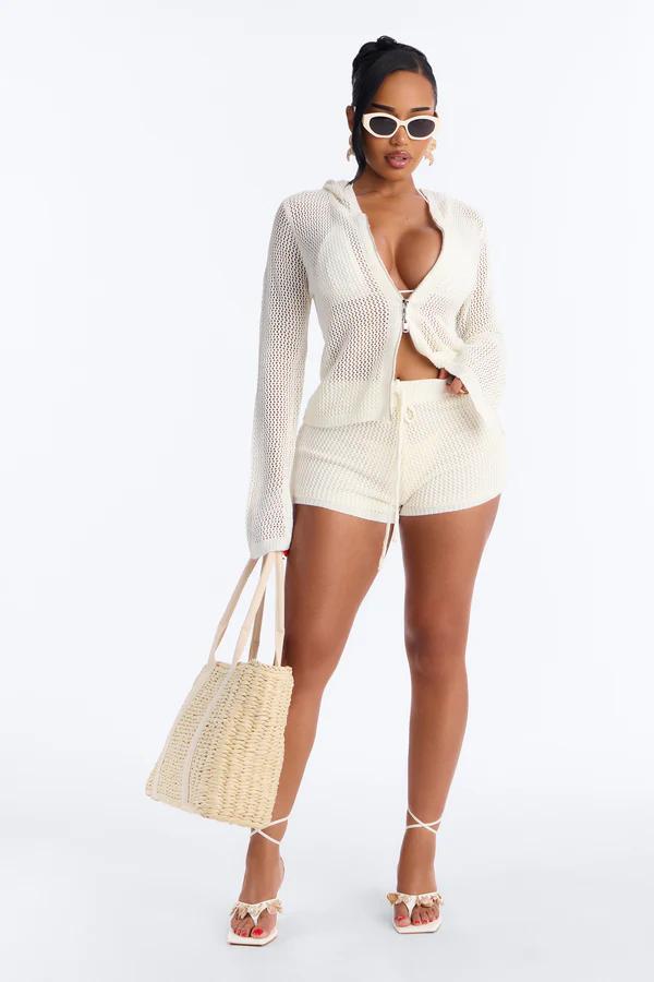 Woman wears a beige crochet strapless crop top with gold ring and a matching open-knit maxi skirt with ruffles.