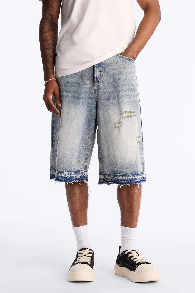 Person models light blue distressed denim shorts with frayed hems, white tee, and black sneakers. Perfect for men's casual summer style.