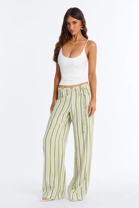 Woman in a white ribbed crop top and high-waisted wide-leg pants with vertical green and beige stripes, standing against a white background.