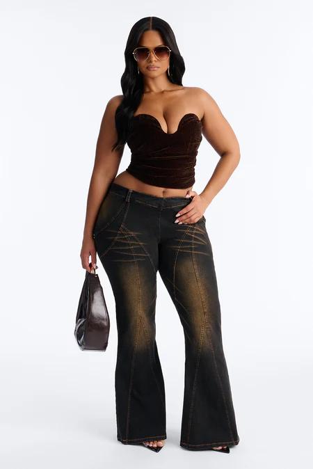 Mujer con gafas de sol doradas, top strapless de terciopelo marrón, jeans acampanados oscuros con deslavado marrón, y bolso pequeño.