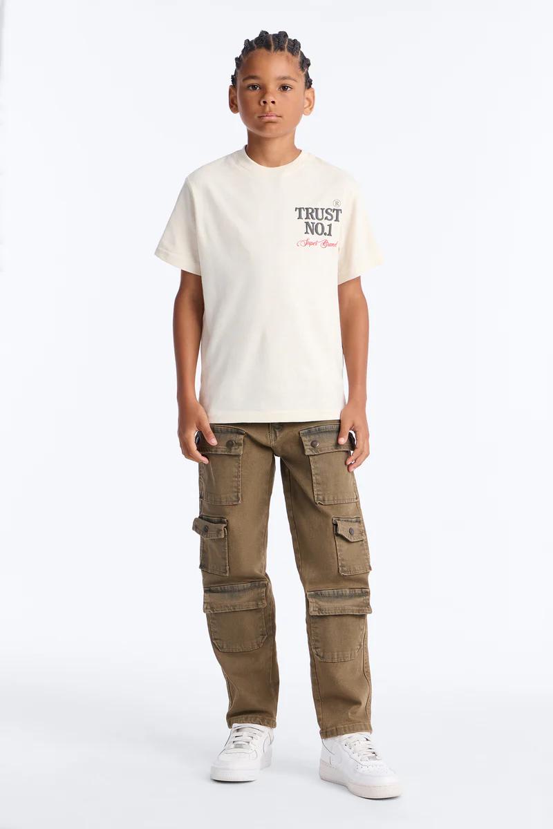 Niño con camiseta crema 'TRUST NO.1' y pantalones cargo marrones. Moda infantil.