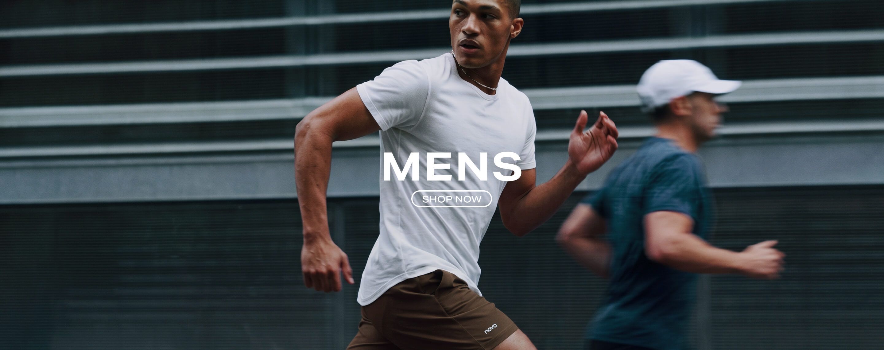 Man running in a white t-shirt and brown athletic shorts. Text overlay reads 'MENS SHOP NOW' to shop the men's workout apparel collection.