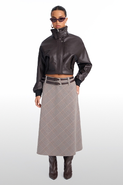 Model wearing a dark brown cropped leather bomber jacket and plaid midi skirt with boots, showcasing the new autumn fashion collection.