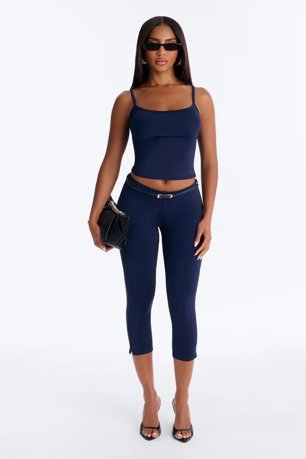 Stylish woman wearing a navy cami crop top, coordinating capri leggings, thin belt, and black sunglasses, holding a purse. Shop the look.