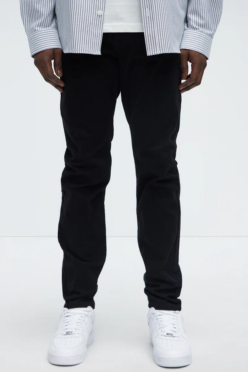 Pantalones negros slim-fit para hombre, usados con camisa de rayas y zapatillas blancas. Descubre ropa casual versátil y básicos.