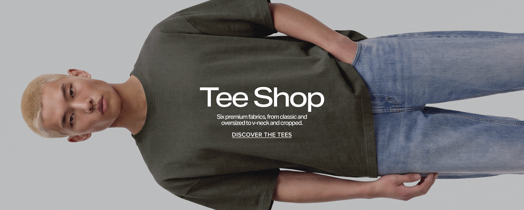 Blonde man in a dark green oversized t-shirt promoting the new Tee Shop collection of premium fabrics. Text reads: Discover the Tees.