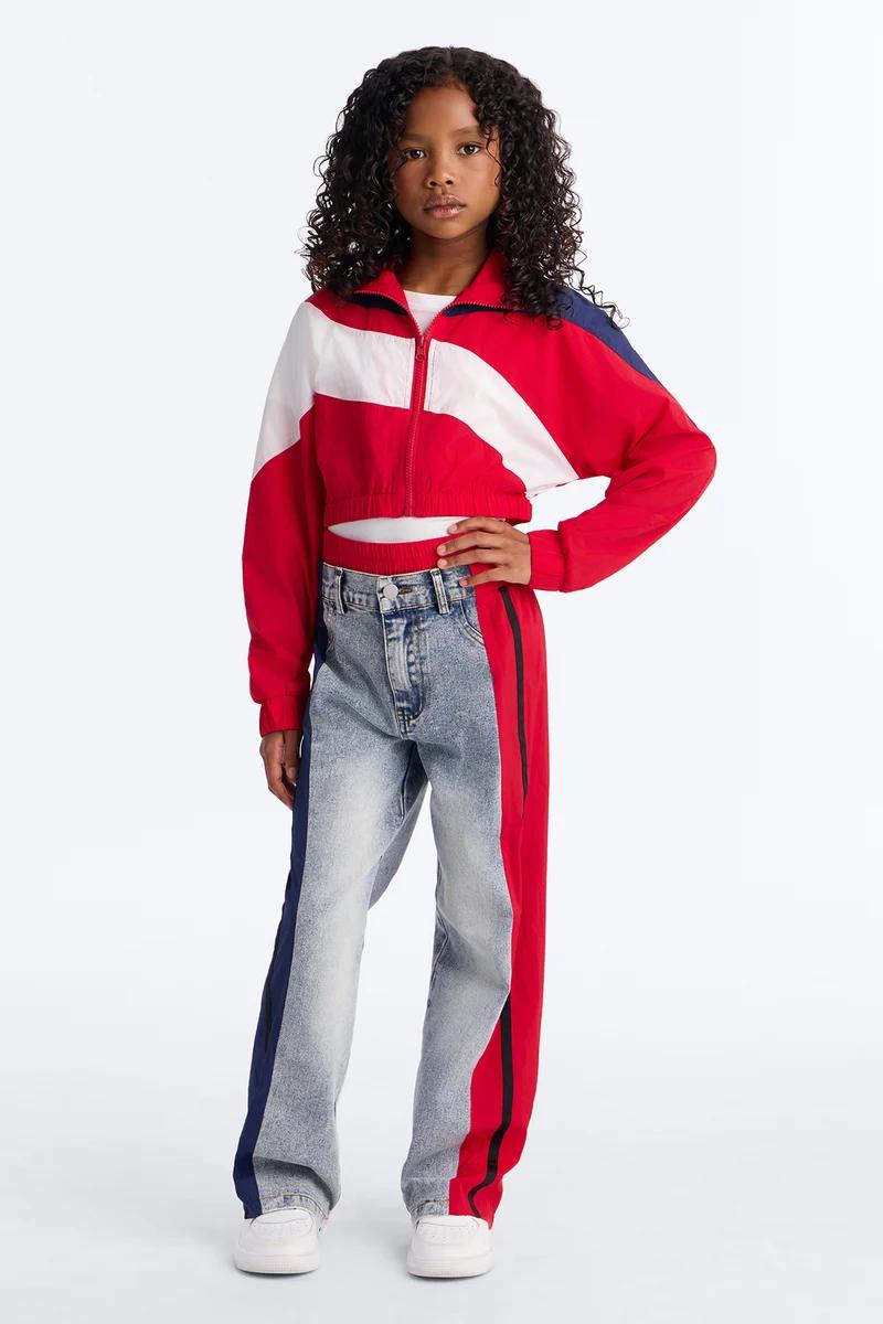 Girl wearing a kids red, white, and blue cropped windbreaker jacket and matching side-stripe hybrid denim jeans.
