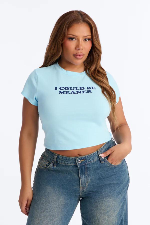 Woman in a light blue crop top with "I COULD BE MEANER" text in dark blue, paired with blue baggy jeans, standing against a white background.
