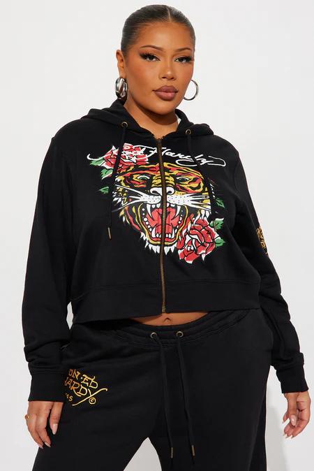 Mujer en sudadera con capucha cropped negra Ed Hardy con gráfico de tigre feroz y rosas rojas, pants a juego con logo dorado.