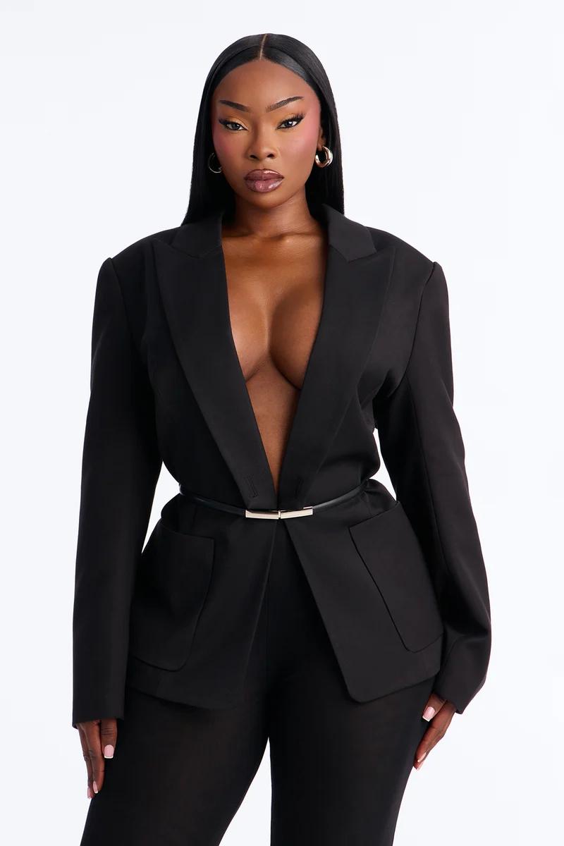 Elegant black woman in a tailored black pant suit with a deep V-neck blazer and slim gold belt.