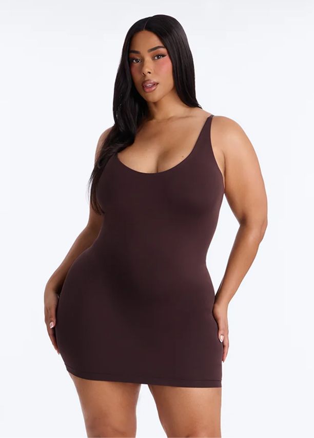 Curvy model wears a seamless brown shapewear slip dress with spaghetti straps against a white backdrop, showcasing the new curve-defining fit.
