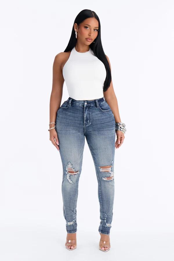 Modelo con top corto halter blanco y jeans ajustados de tiro alto desgastados, mostrando una propuesta de moda casual para mujer.the crust is 